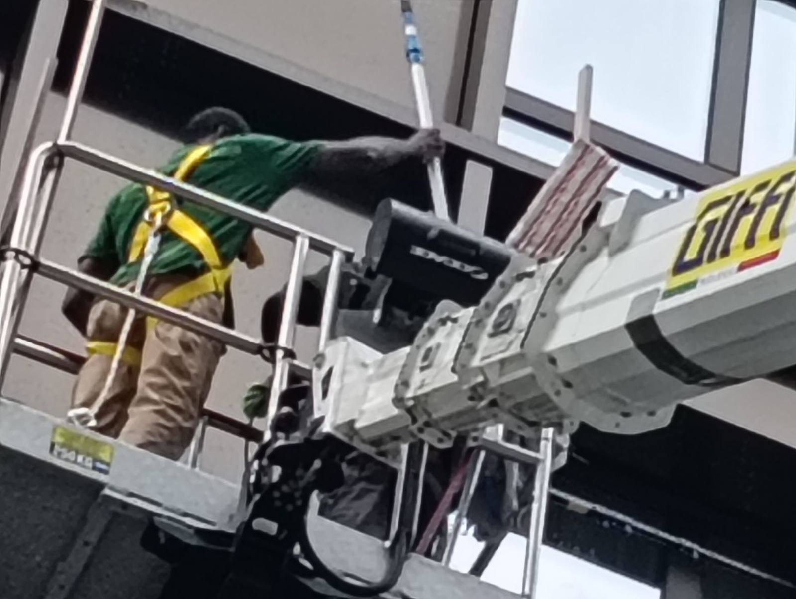 Operatore su piattaforma aerea mentre lava una vetrata con asta telescopica